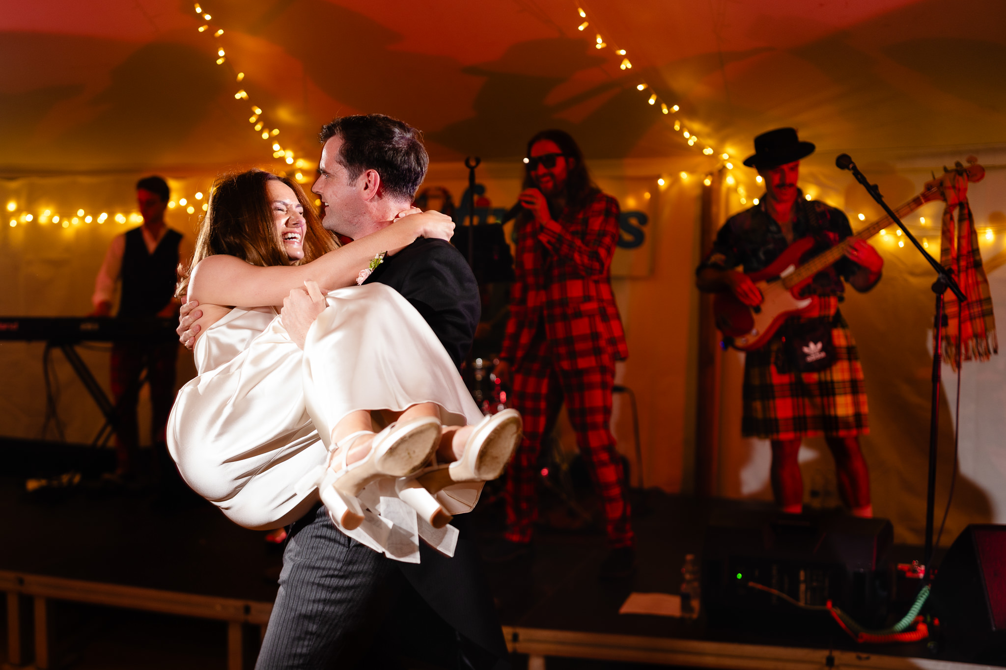 Groom carrying his laughing bride across the dancefloor in front of the band
