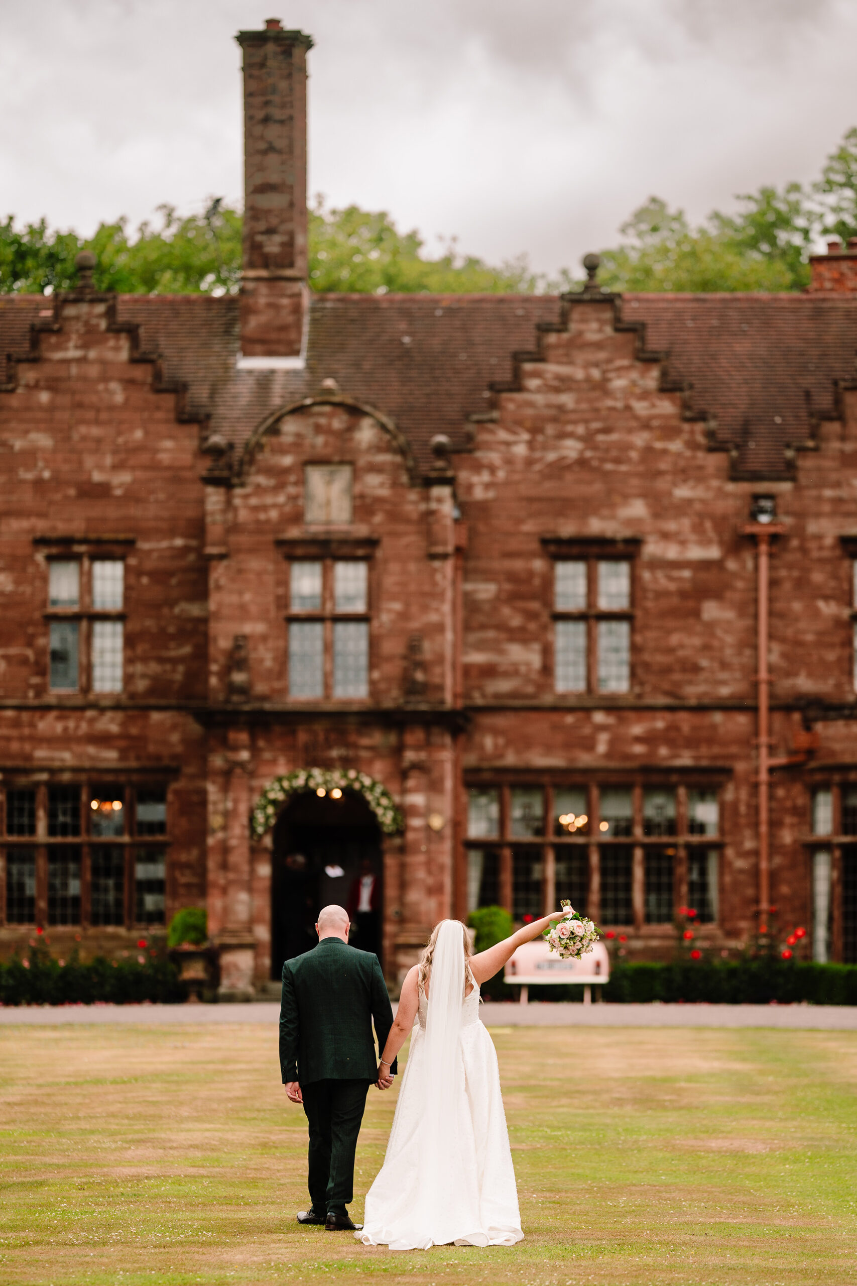 Chloe and Pete walking hand in hand across the lawn with Wrenbury Hall behind them