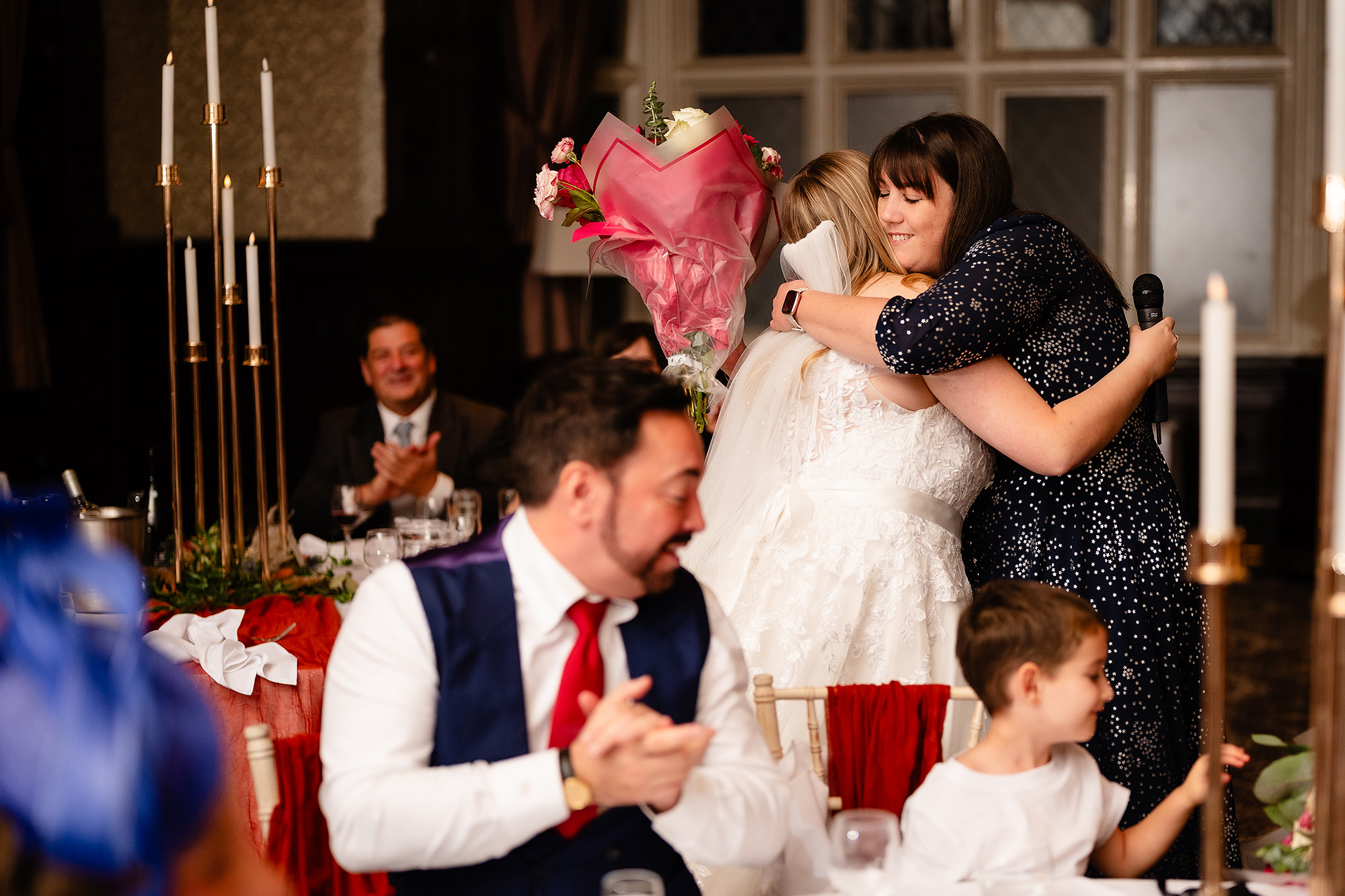 Annie being hugged after her speech, flowers in hand, Crewe Hall wedding photographer