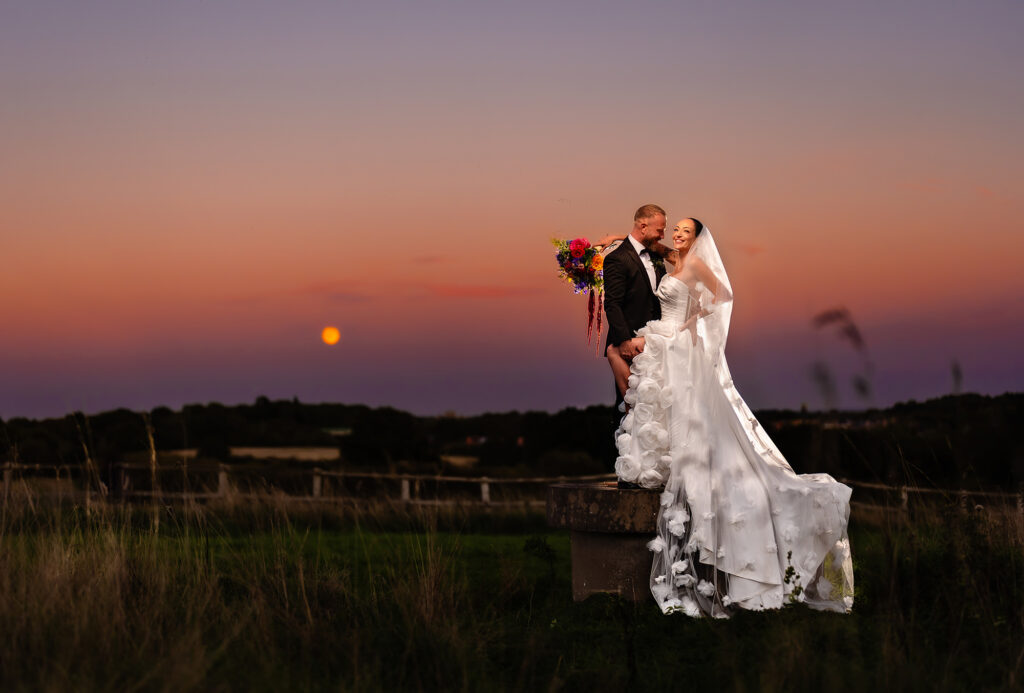 Kim and Glynn on a stone bench under a pink dusk sky with the moon low on the horizon, Nottingham wedding photographer