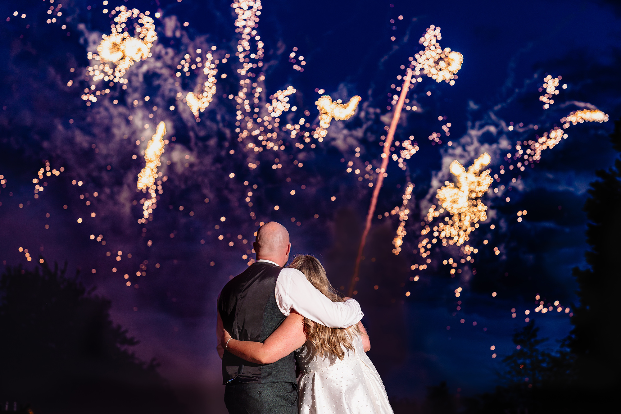 A wide shot of fireworks filling the sky over Chloe and Pete’s silhouette at Wrenbury Hall
