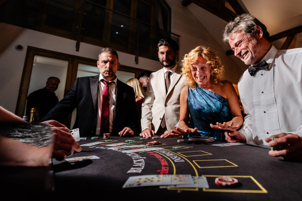 Guests laughing around the blackjack table at the evening casino, Swancar Farm wedding photographer