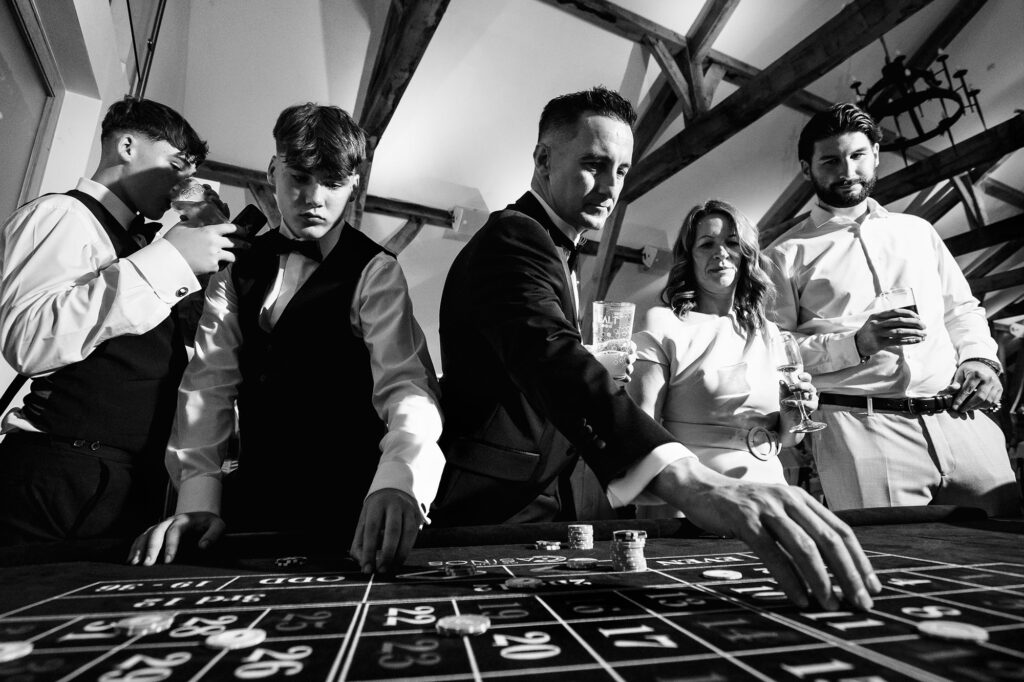 Black and white of guests placing chips at the roulette table, Swancar Farm wedding photographer