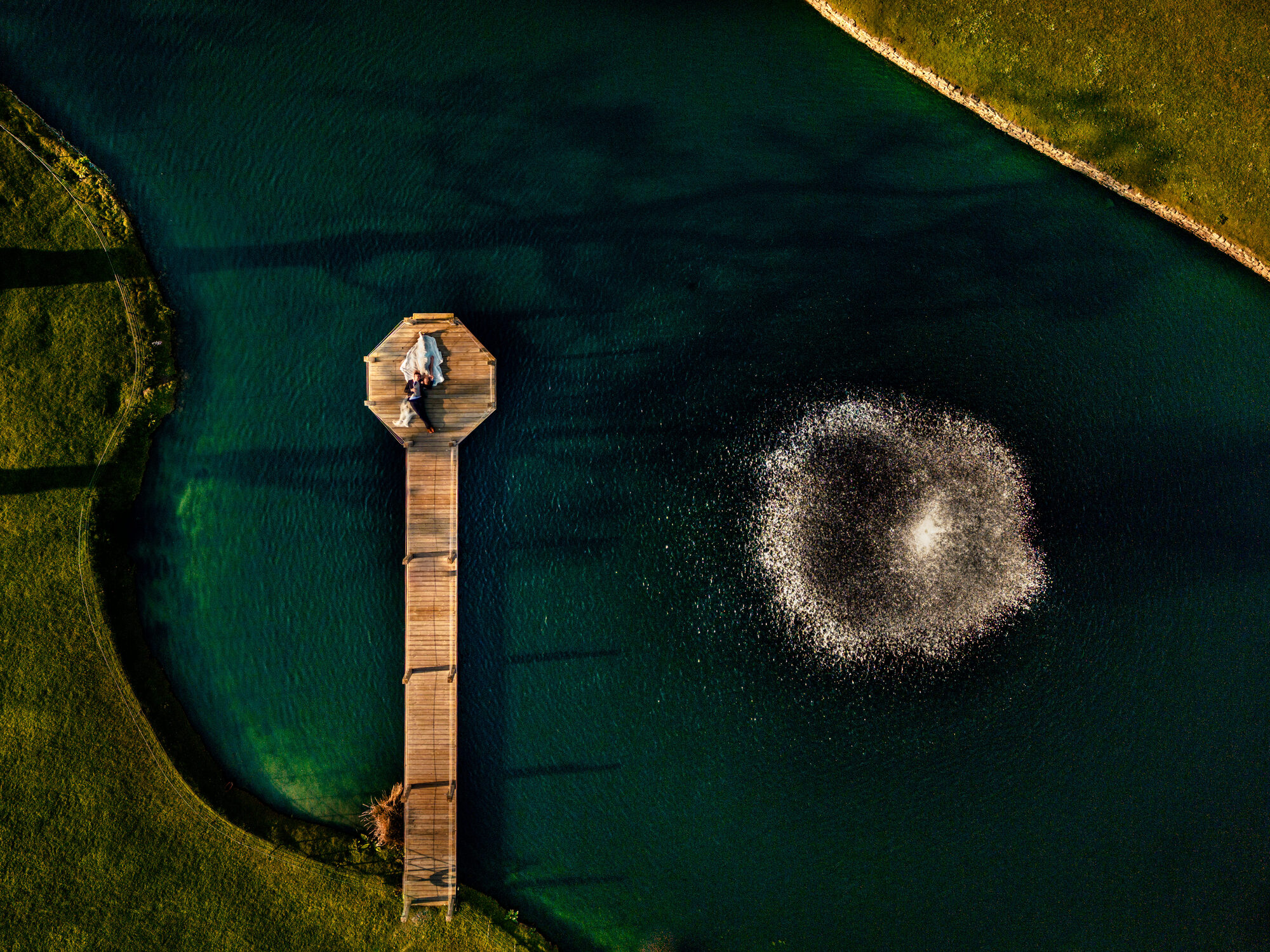 Bride and groom on a jetty beside a lake, photographed from above