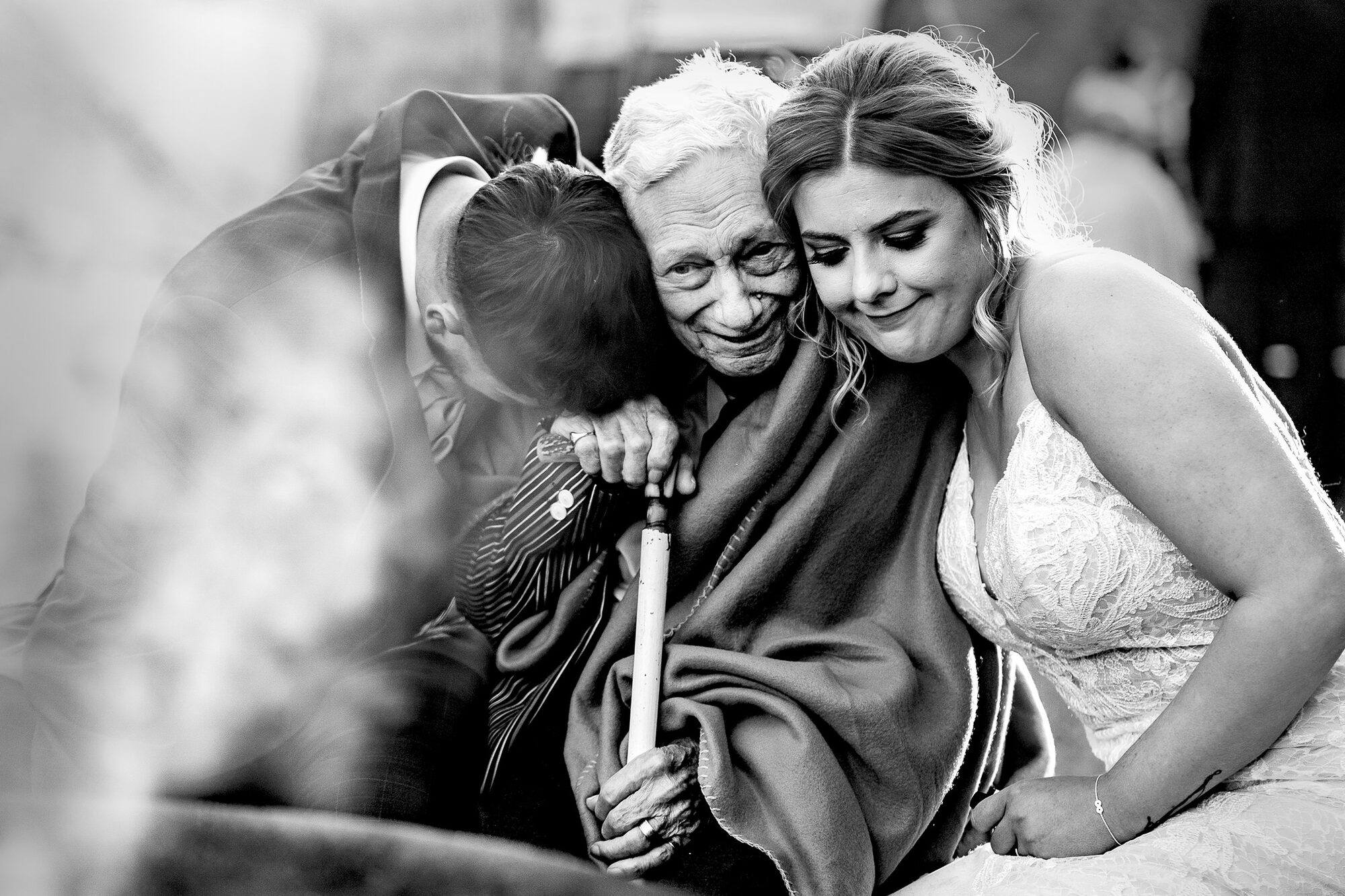 Black and white photograph of a bride and groom hugging her grandmother
