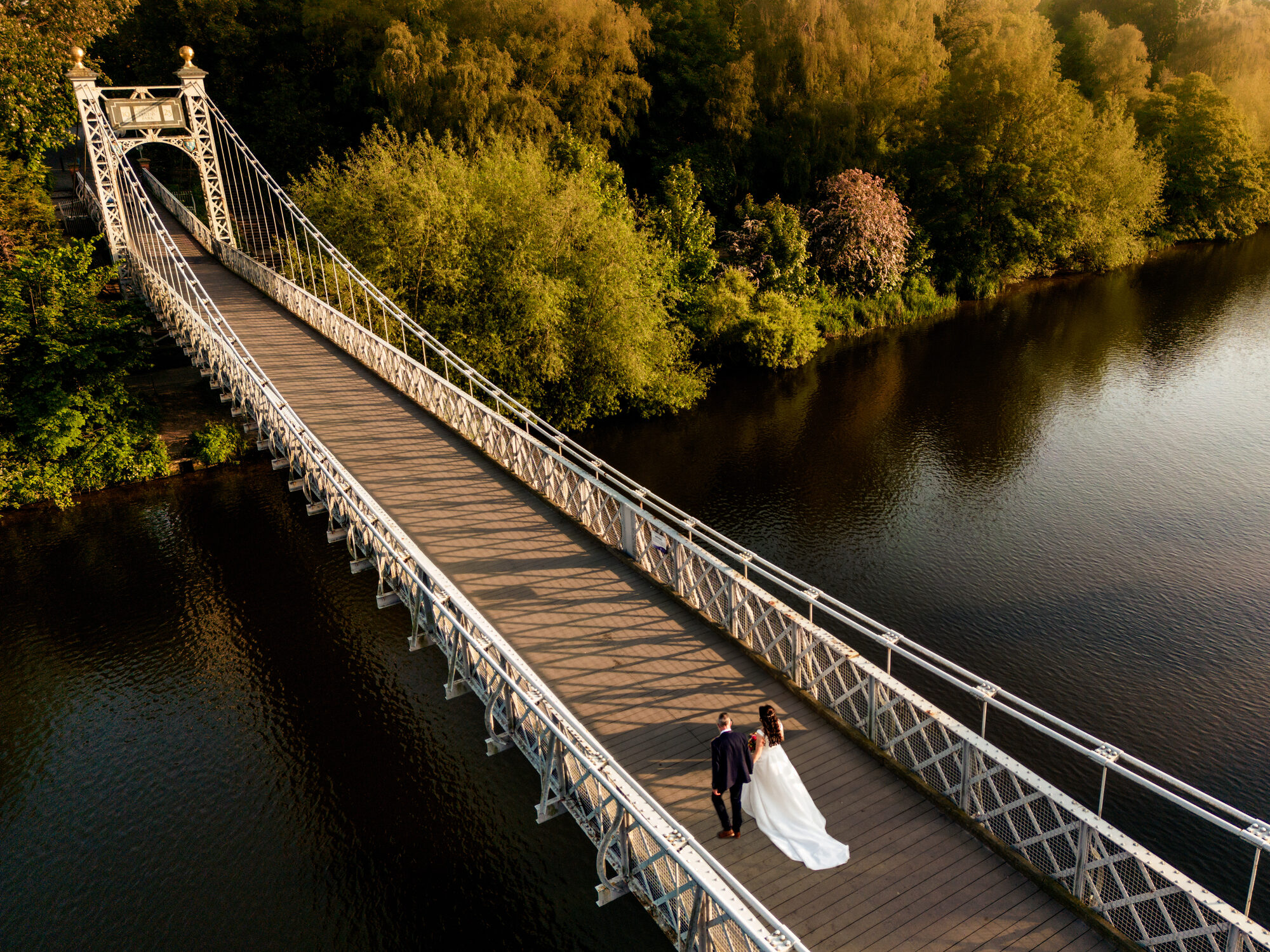 Bride and groom alone on a suspension bridge over the river