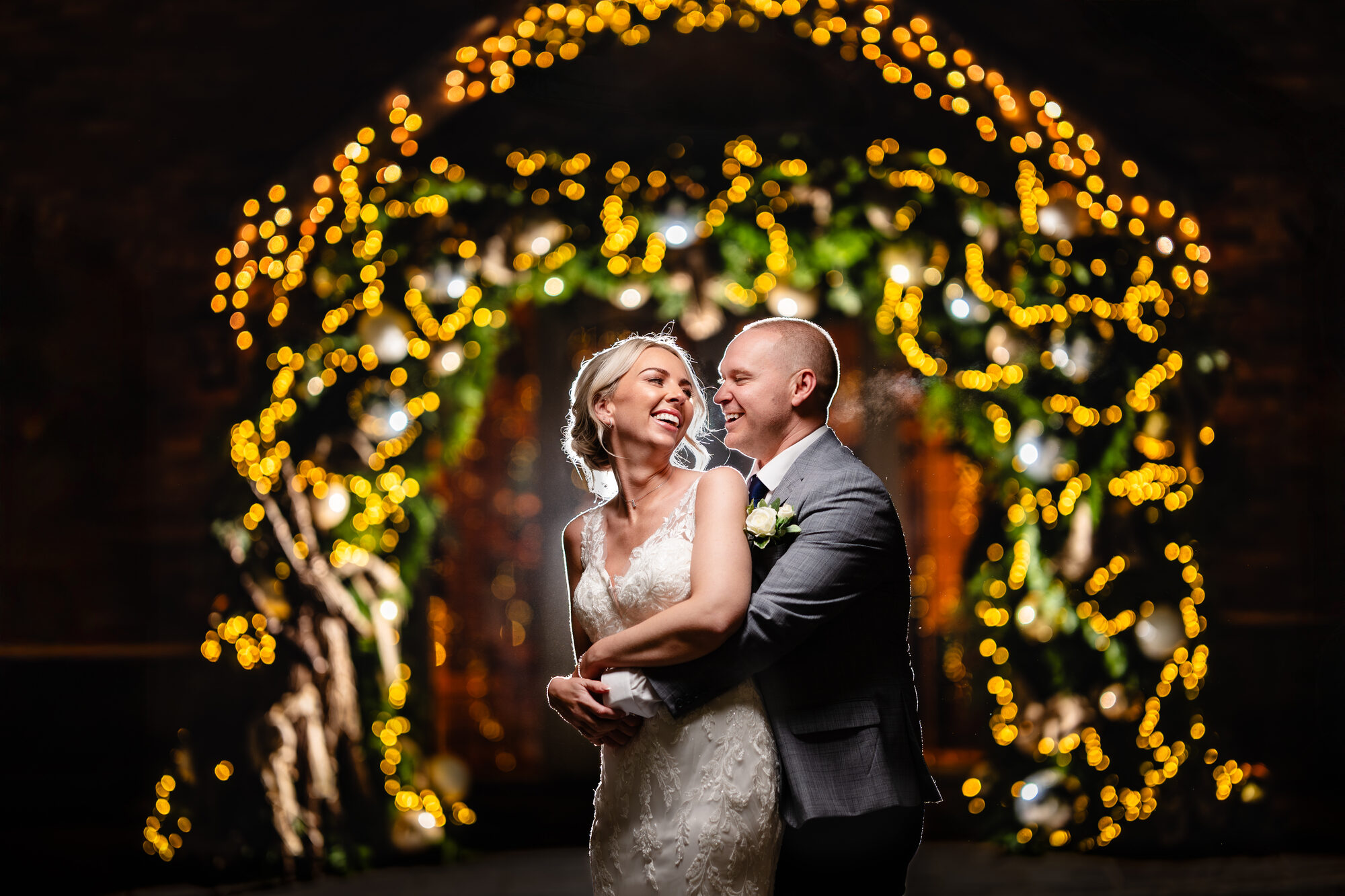 Bride and groom under an archway of golden fairy lights