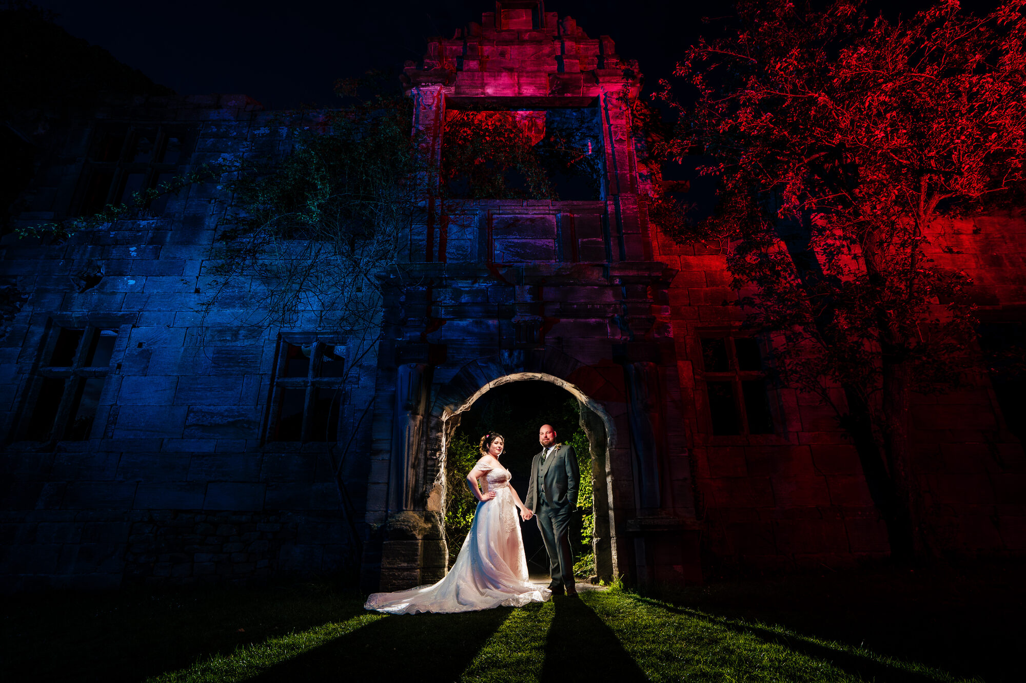 Bride and groom in an archway of a castle uplit in red and blue