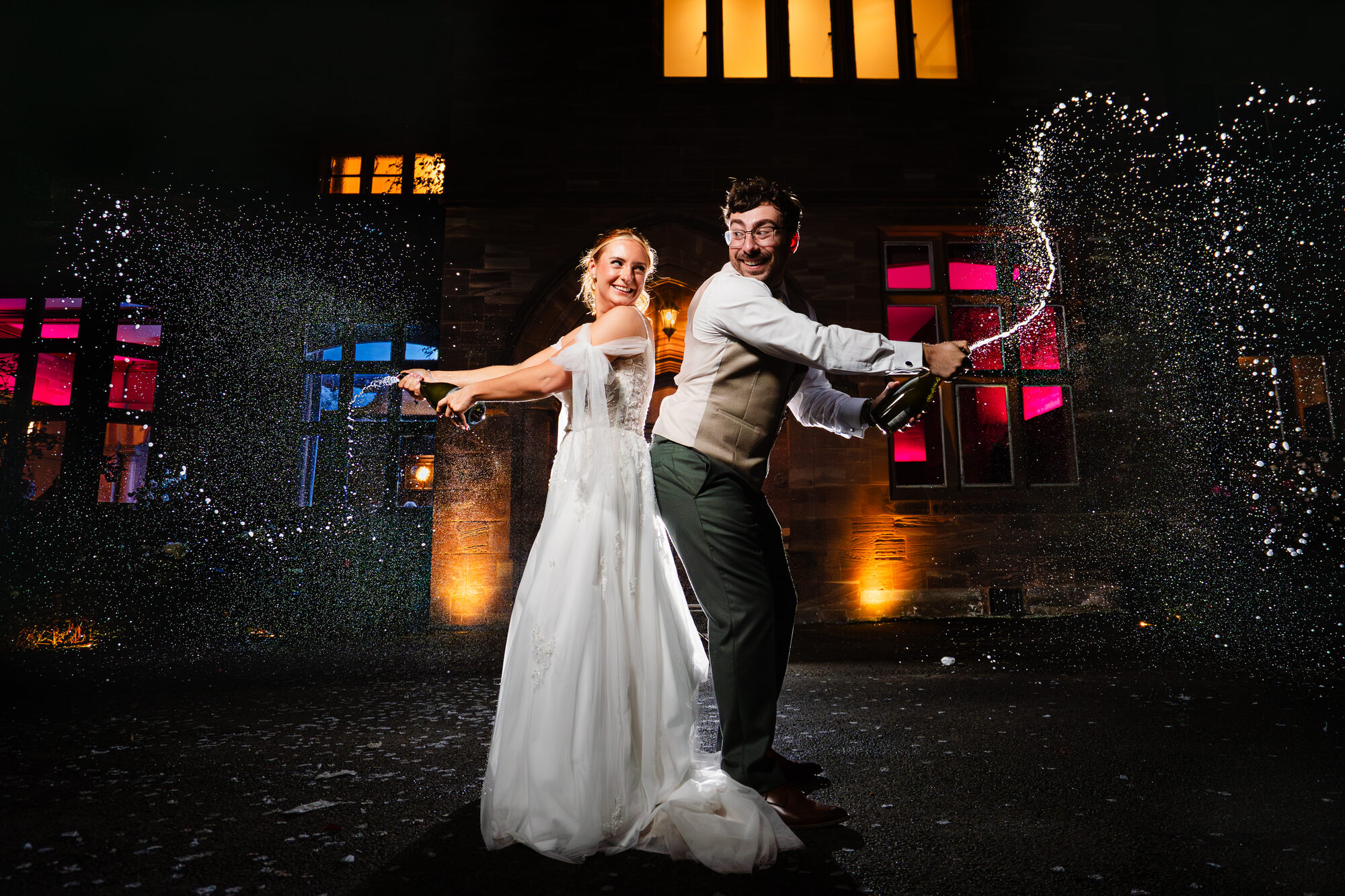 Champagne sprayed in front of a floodlit wedding venue at night
