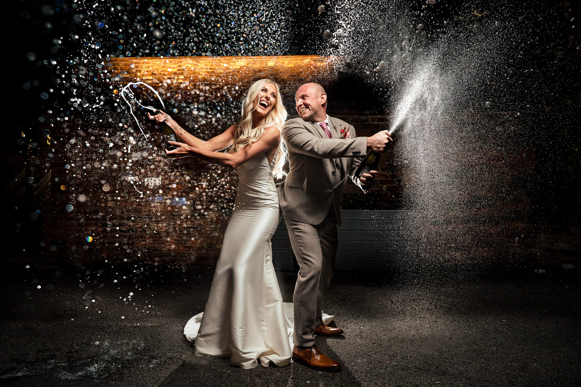 Bride and groom spraying champagne, lit by flash at night