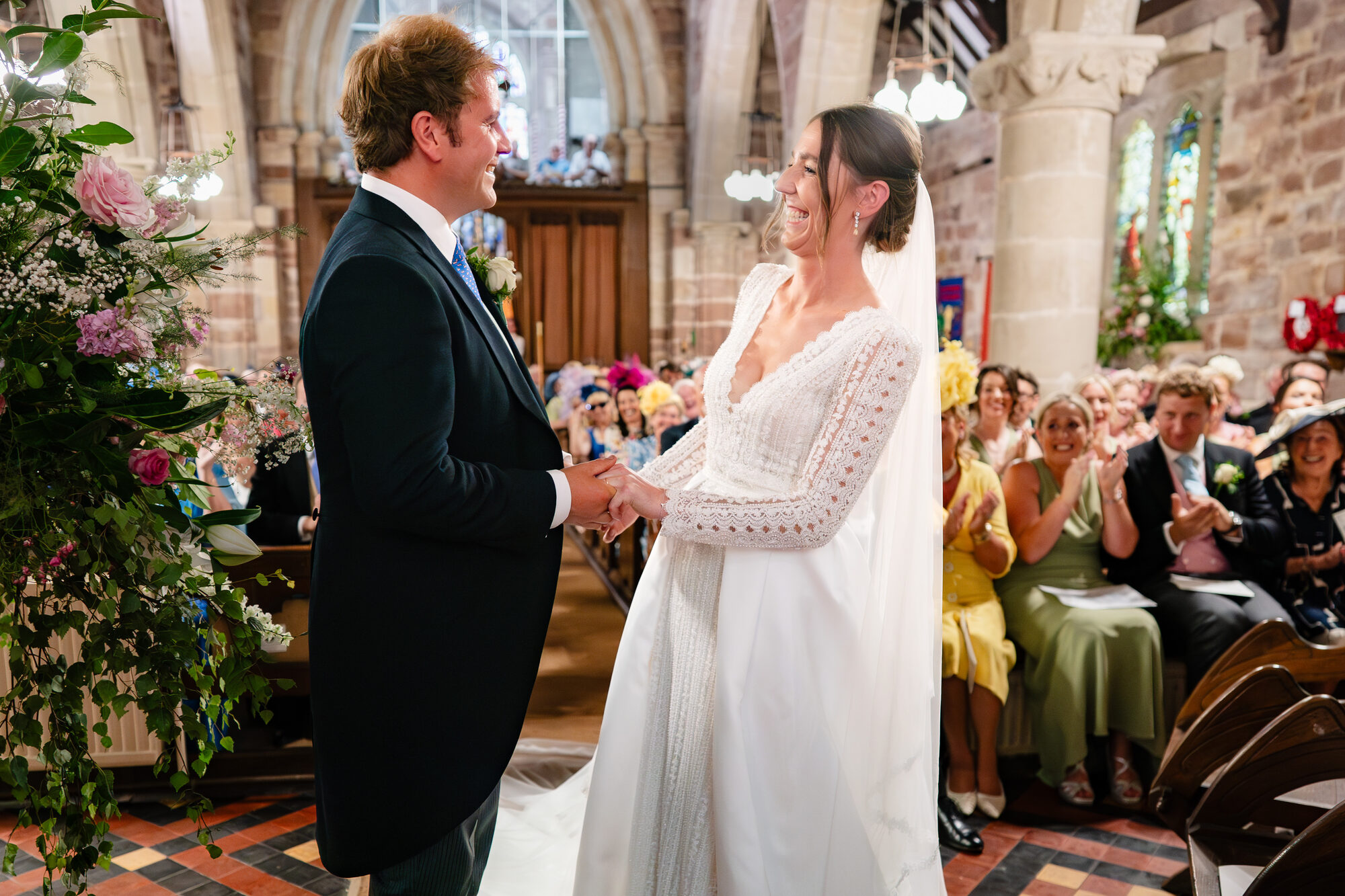 Bride and groom holding hands during their vows under a church flower arch