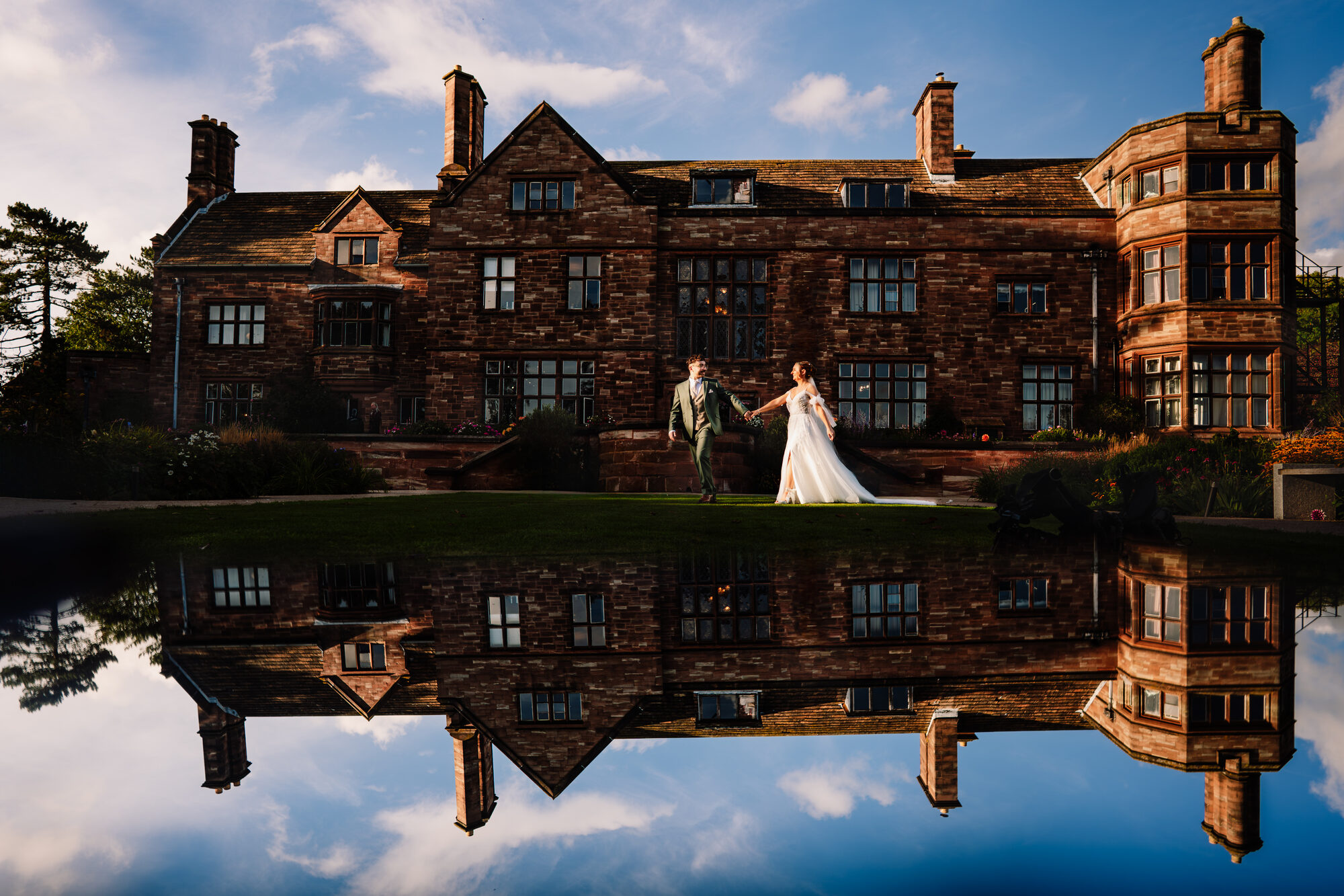 Bride and groom in front of a country house, mirrored in still water
