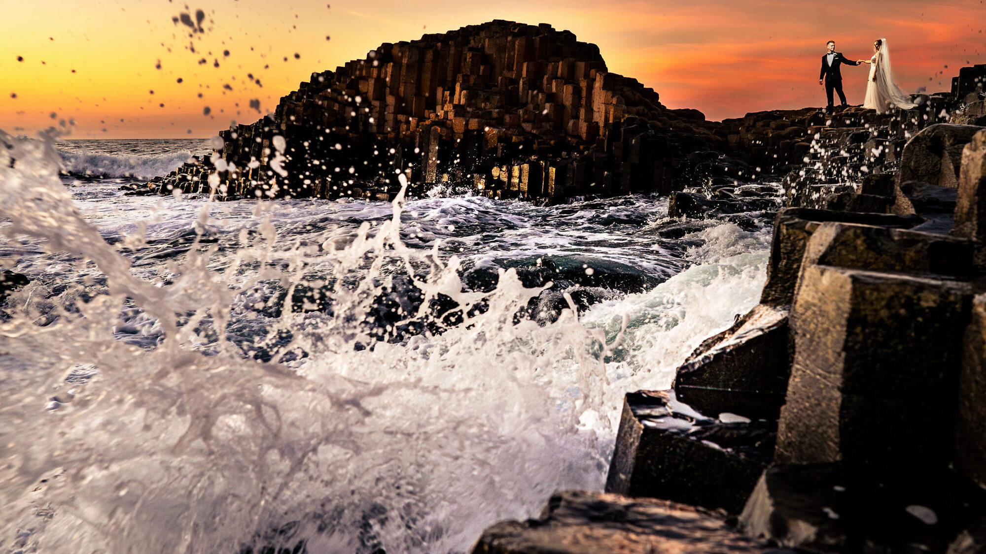Bride and groom on the Giant's Causeway as waves crash below them