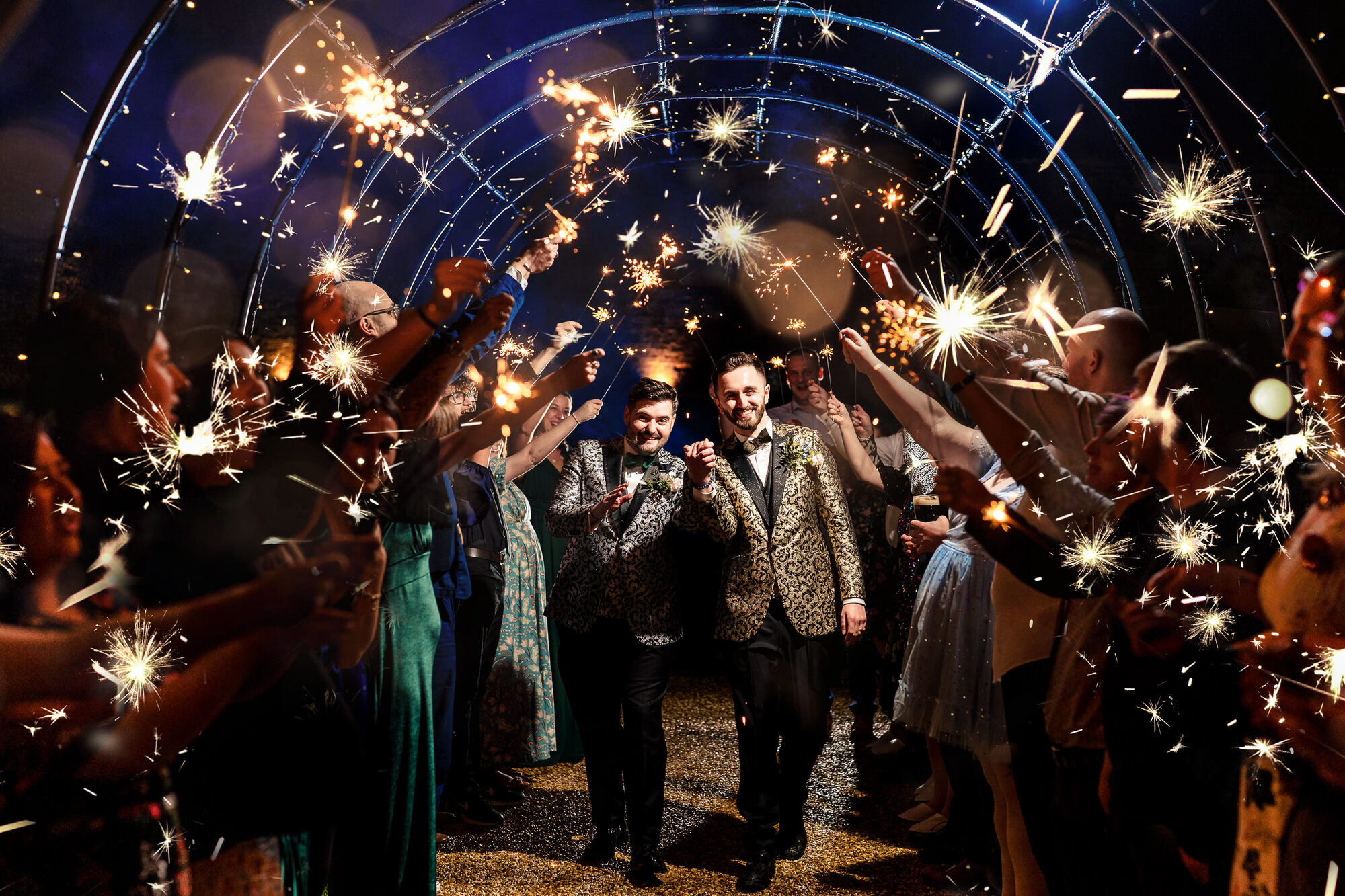Guests holding sparklers overhead as the couple walk through