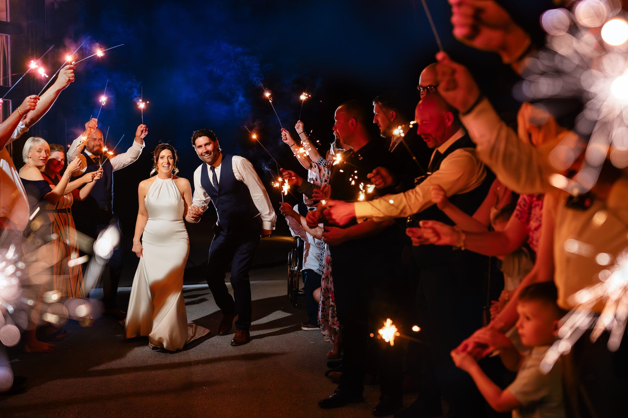 Couple running through a tunnel of sparklers and blue smoke
