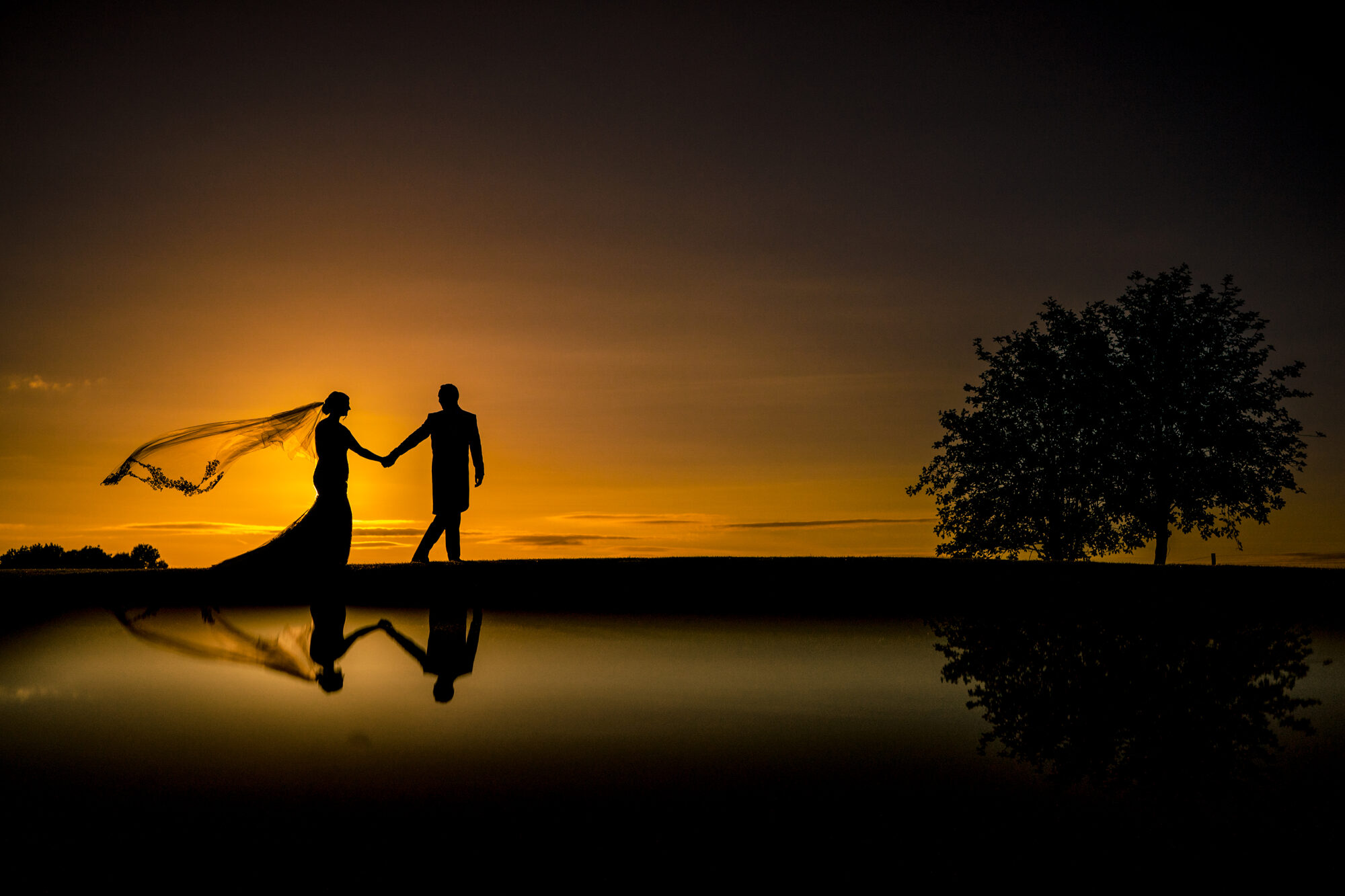 Bride and groom silhouetted at sunset with her veil catching the wind