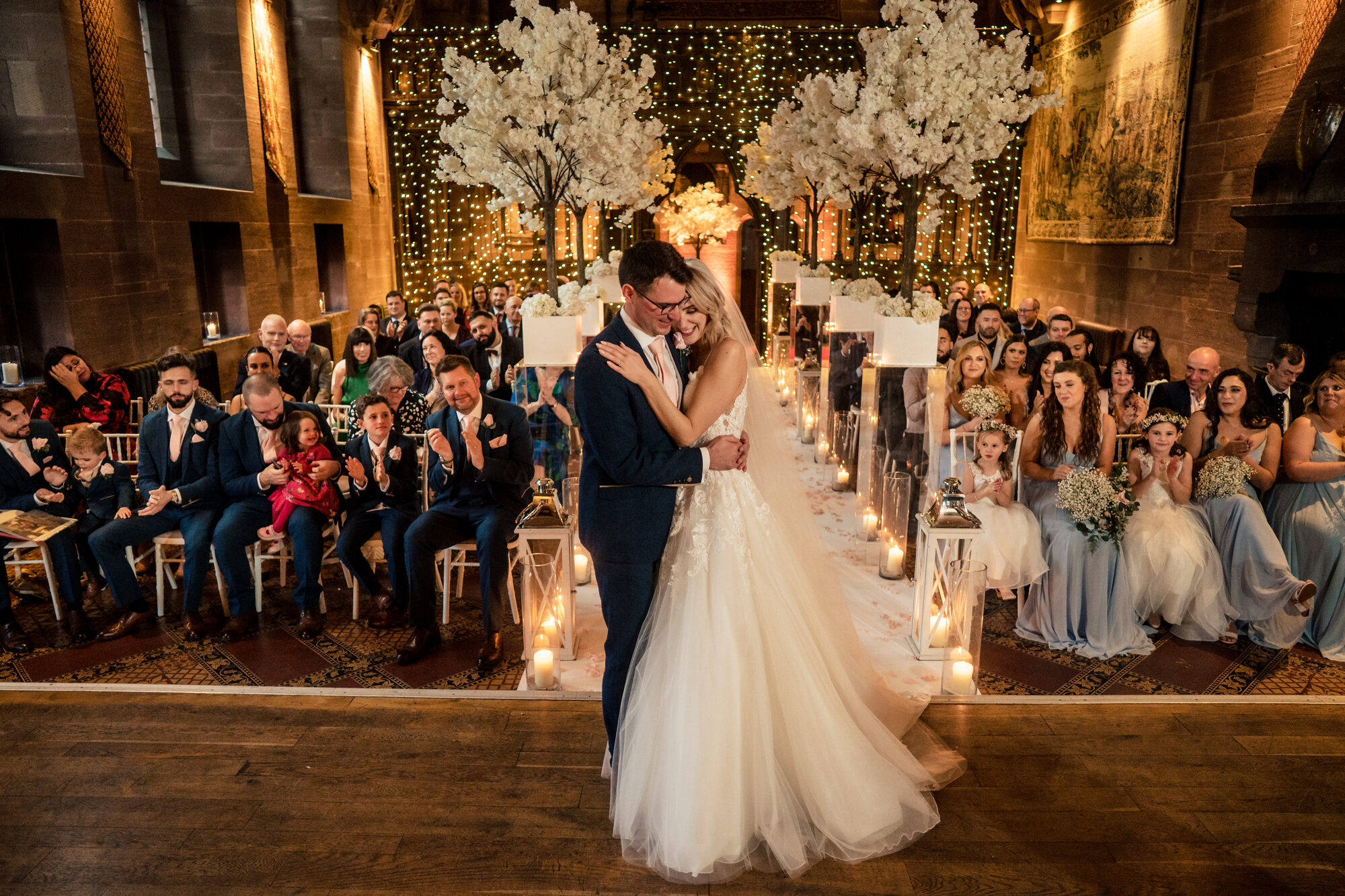 Bride and groom exchanging vows in a candlelit hall filled with blossom trees