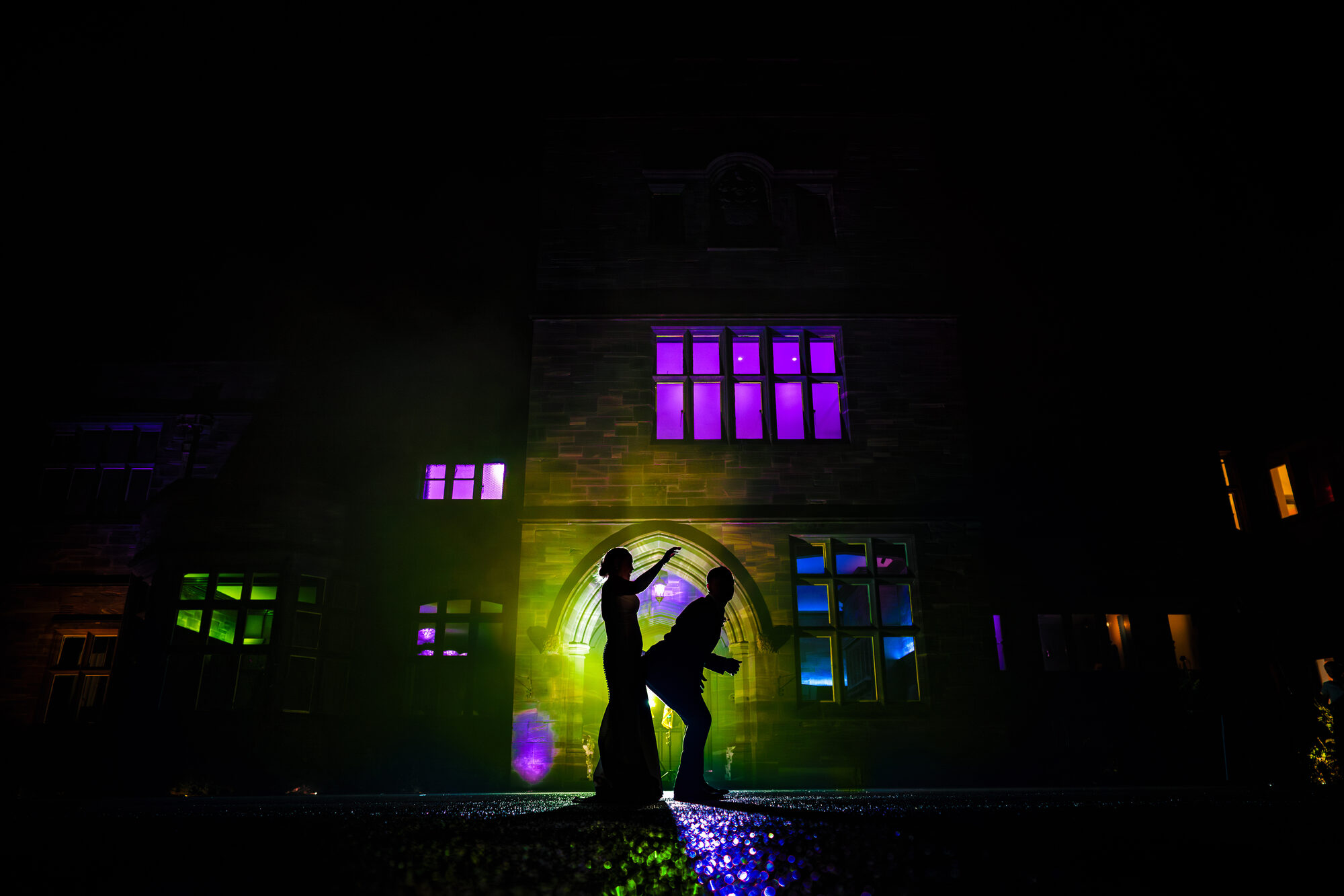Bride and groom silhouetted against a wedding venue lit in purple and green