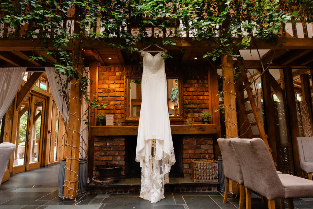 Lace wedding dress hanging beneath ivy covered oak beams in front of a brick fireplace at The Oak Tree of Peover