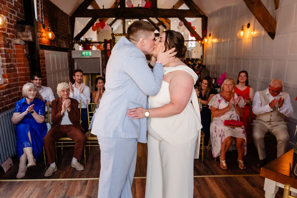 Marianne and Emma kissing during their ceremony as family clap, Knutsford wedding photographer