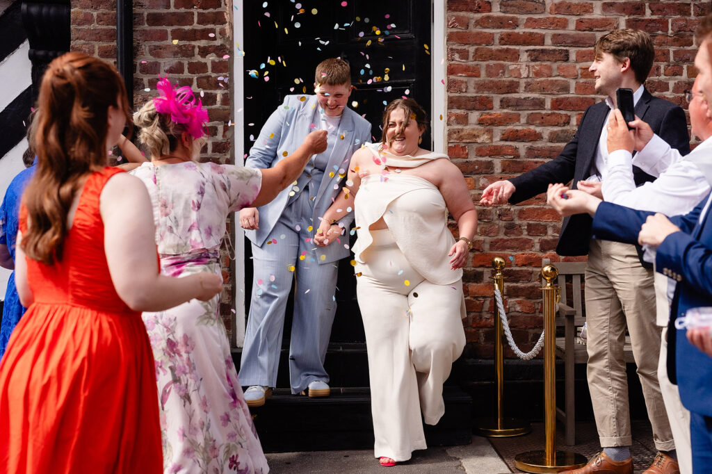 Marianne and Emma stepping out of a black front door into a shower of colourful confetti