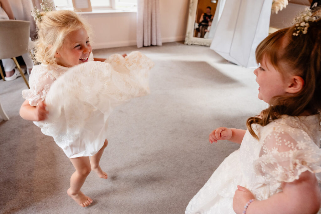 Two flower girls in lace dresses dancing and giggling barefoot in the bridal suite