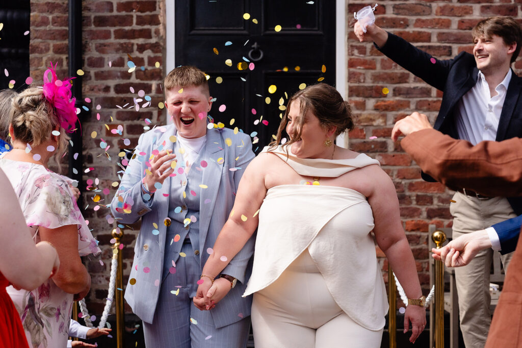 Marianne and Emma laughing hand in hand through colourful confetti, Knutsford wedding photographer