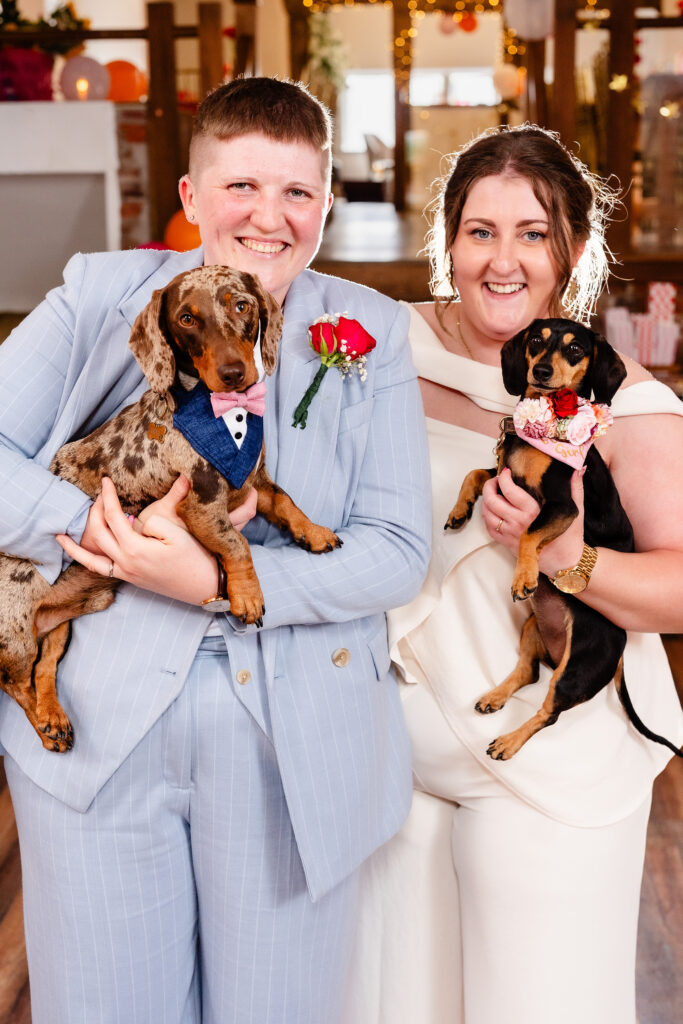 Marianne and Emma each holding one of their sausage dogs, Belle and Brian, at their Knutsford wedding