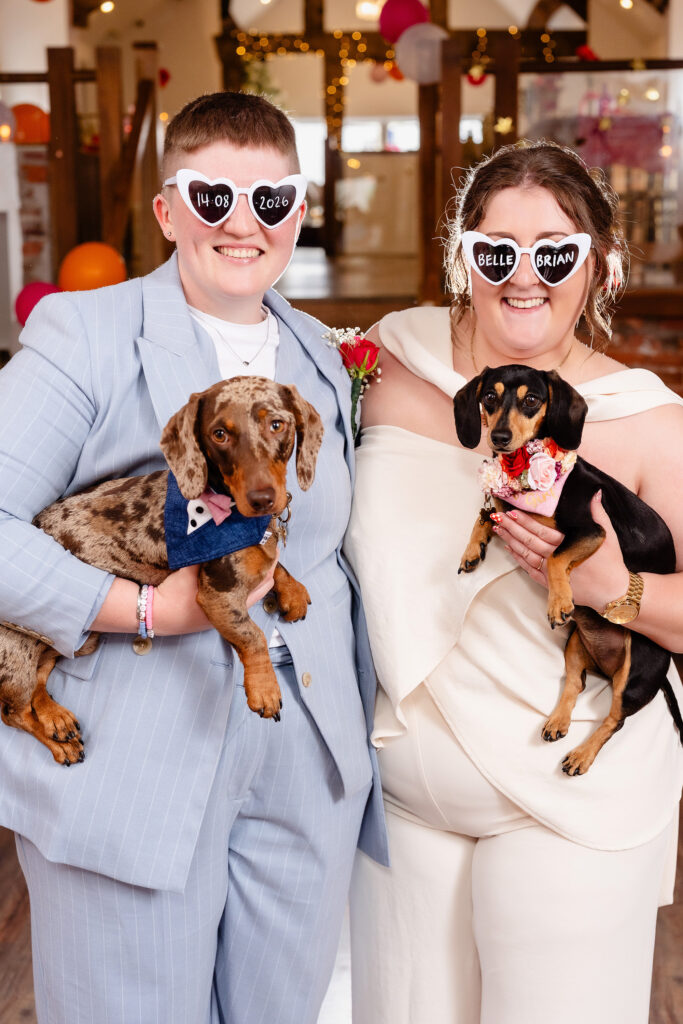 Marianne and Emma in heart shaped sunglasses holding their two sausage dogs, Knutsford wedding photographer