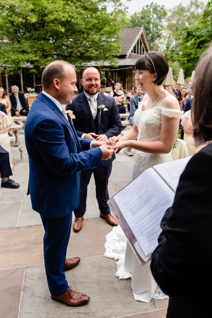 Bride smiling as she exchanges rings with the groom at their outdoor wedding ceremony