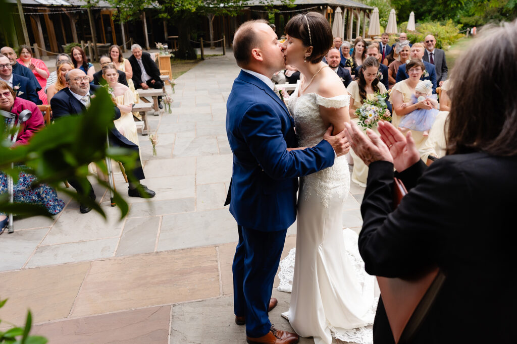 Bride and groom share their first kiss as guests applaud, Cheshire wedding photographer