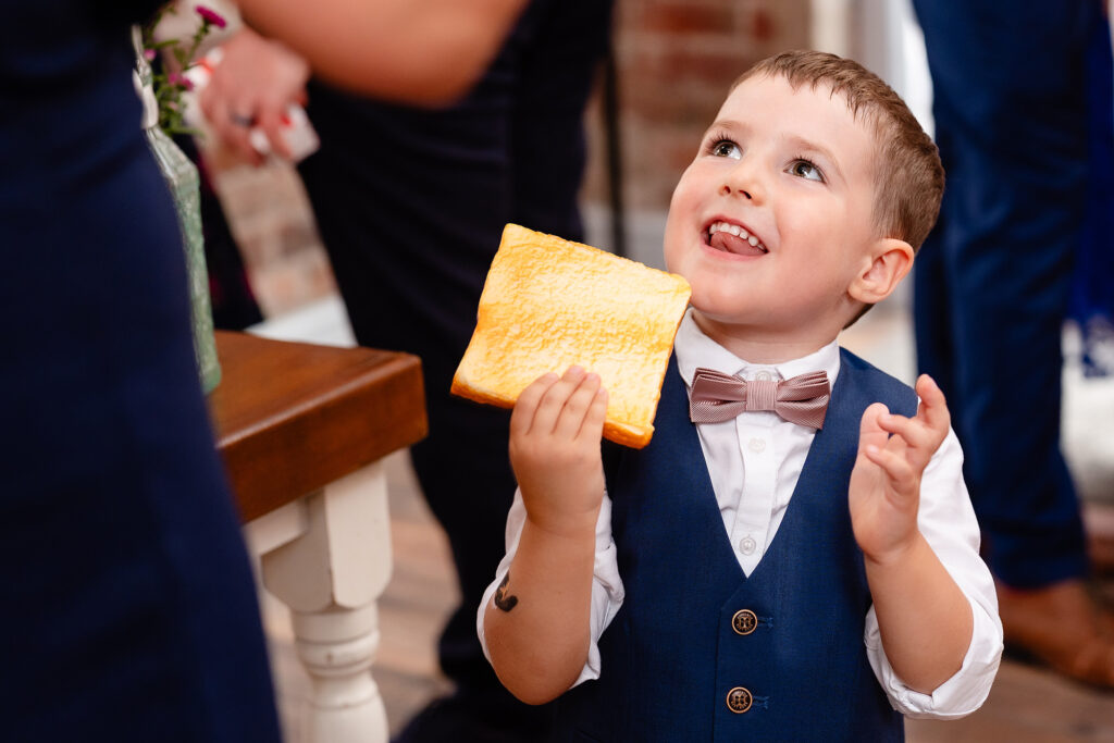 Little boy in a bow tie looking up and grinning, holding a slice of toast