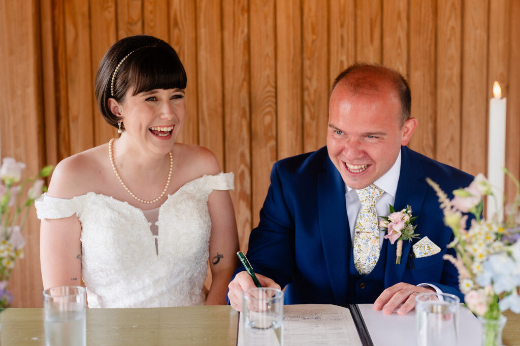 Bride and groom laughing as they sign the wedding register at The Oak Tree of Peover