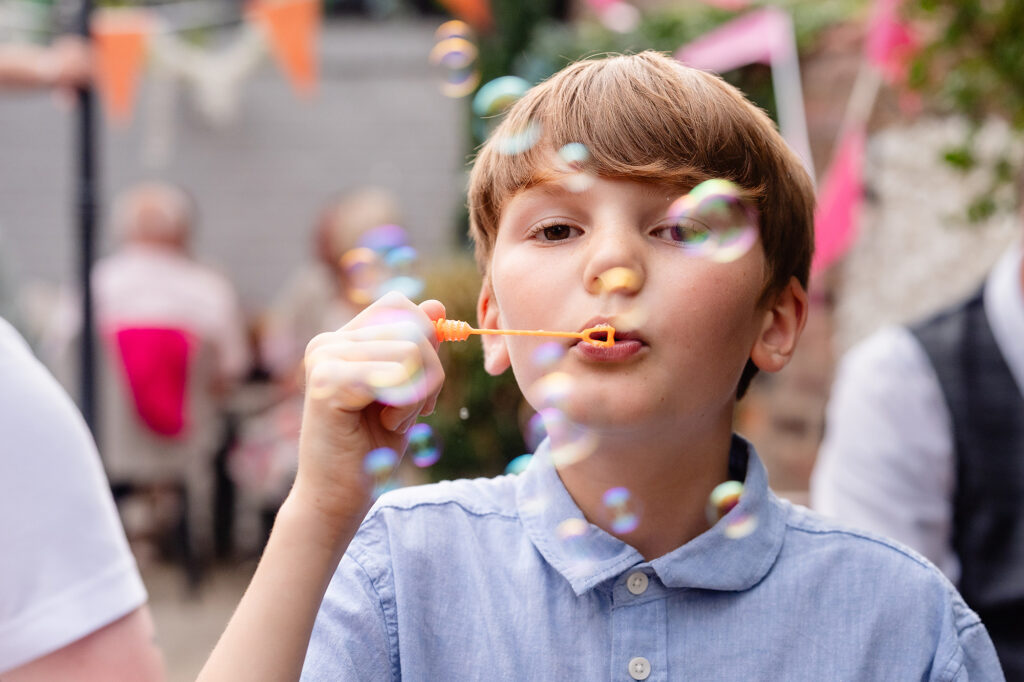 Young guest blowing bubbles under bunting, Knutsford wedding photographer