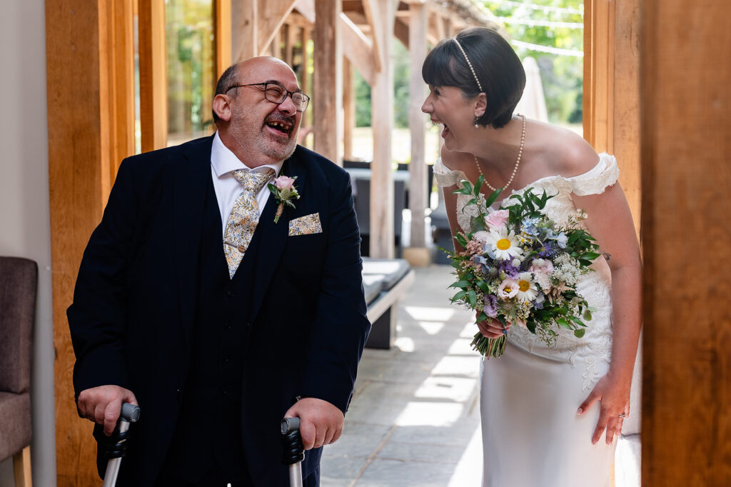 Bride holding her wildflower bouquet and roaring with laughter with a guest in a navy suit