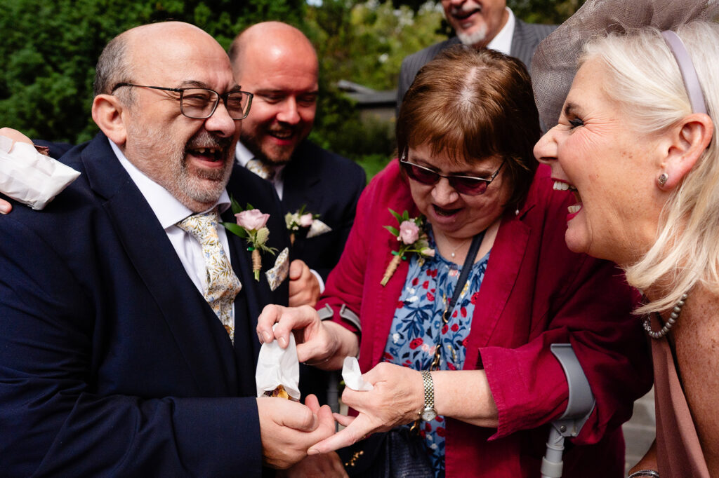Wedding guests in buttonholes laughing together outside after the ceremony
