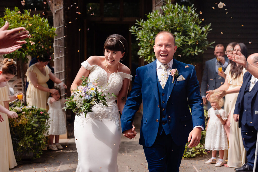 Confetti falling over the laughing bride and groom outside the barn, Cheshire wedding photographer
