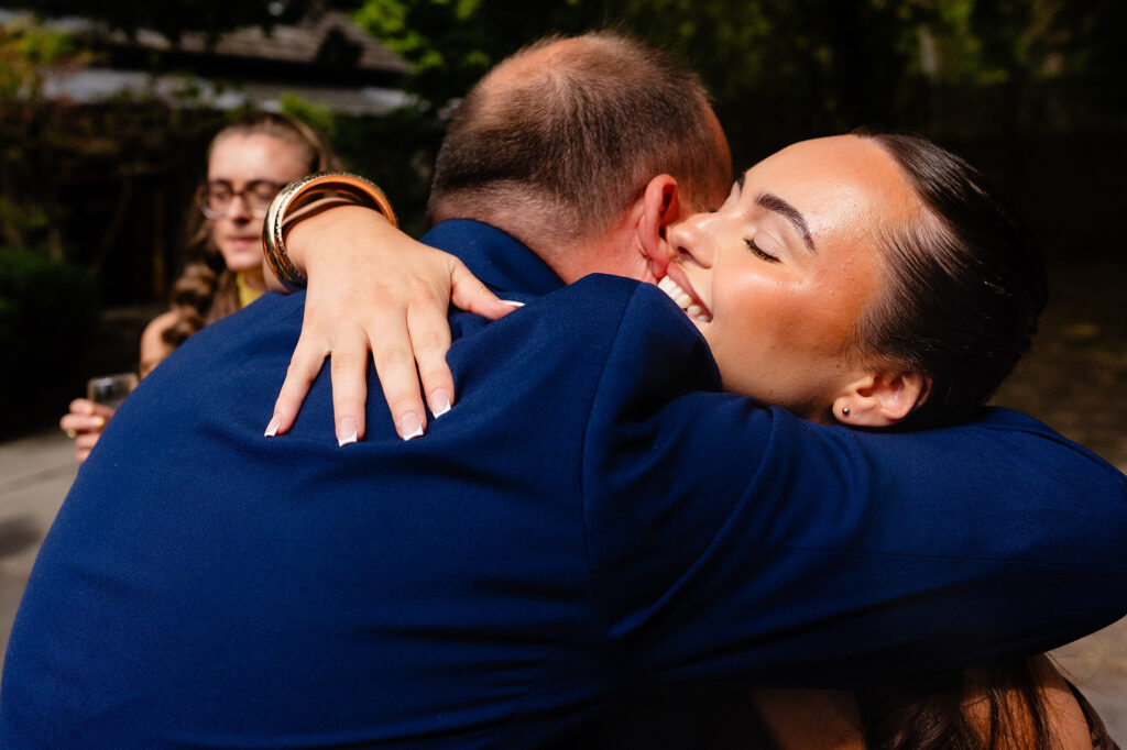 Guest with her eyes closed squeezing a man in a blue suit in a big hug after the confetti