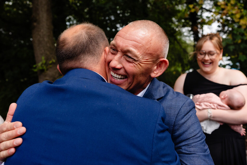 Guest beaming mid hug with a man in a blue suit during the drinks reception