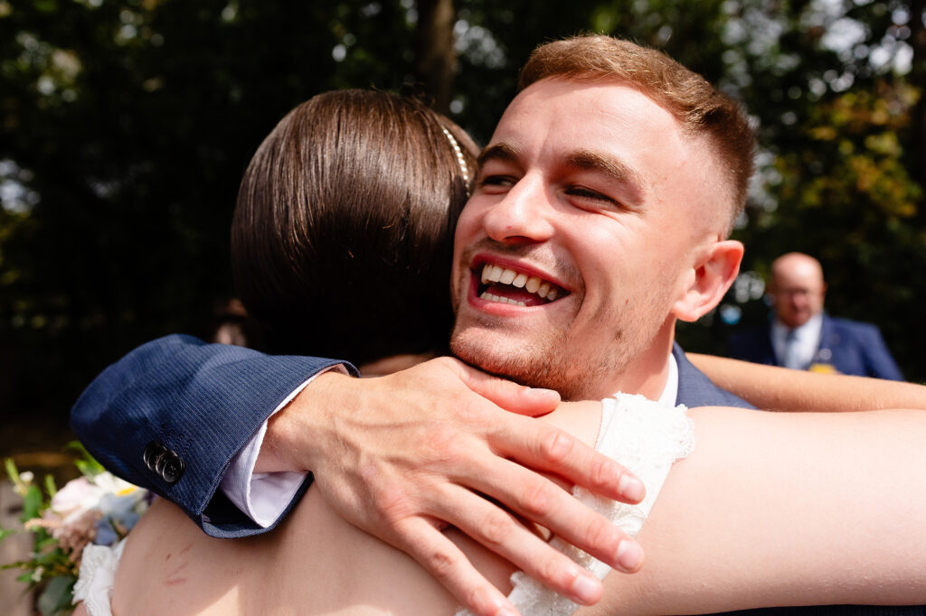 Laughing guest wrapping the bride in a hug during the drinks reception at The Oak Tree of Peover