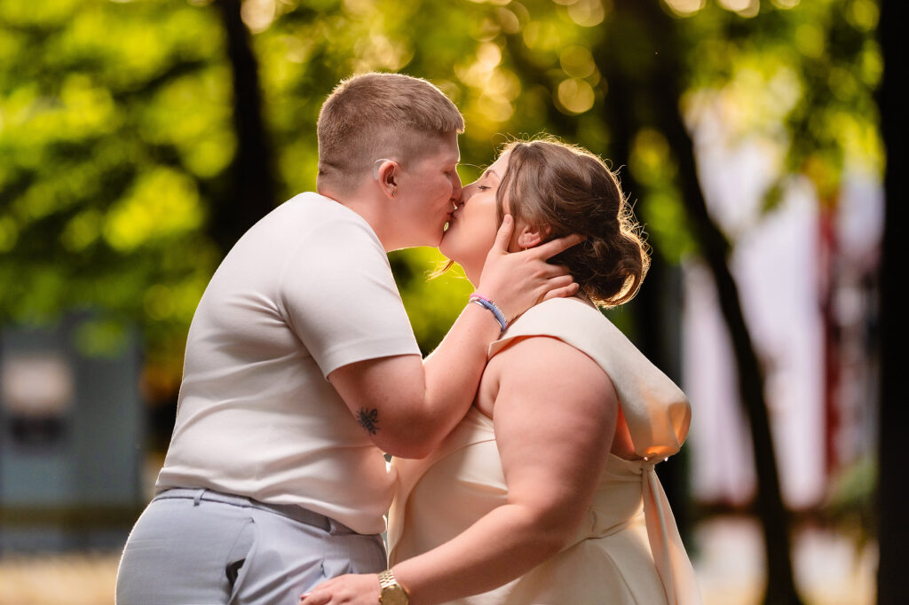 Marianne and Emma kissing with sunlit trees behind them