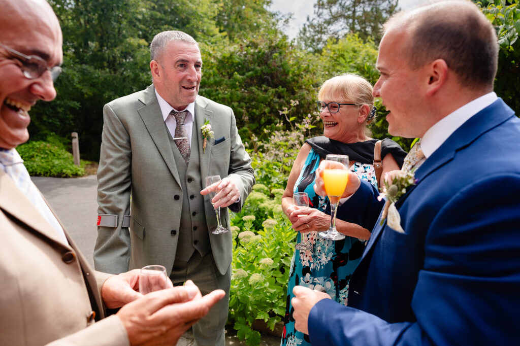 Guests laughing and chatting with drinks in the gardens during the drinks reception