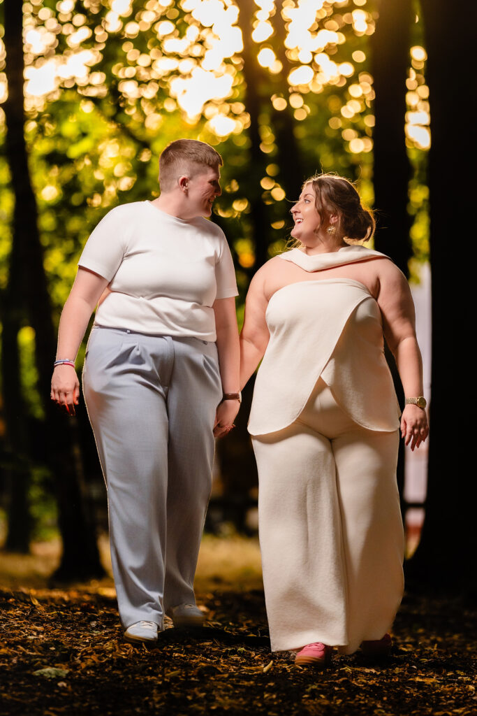 Marianne and Emma walking hand in hand through the trees with the sun behind them