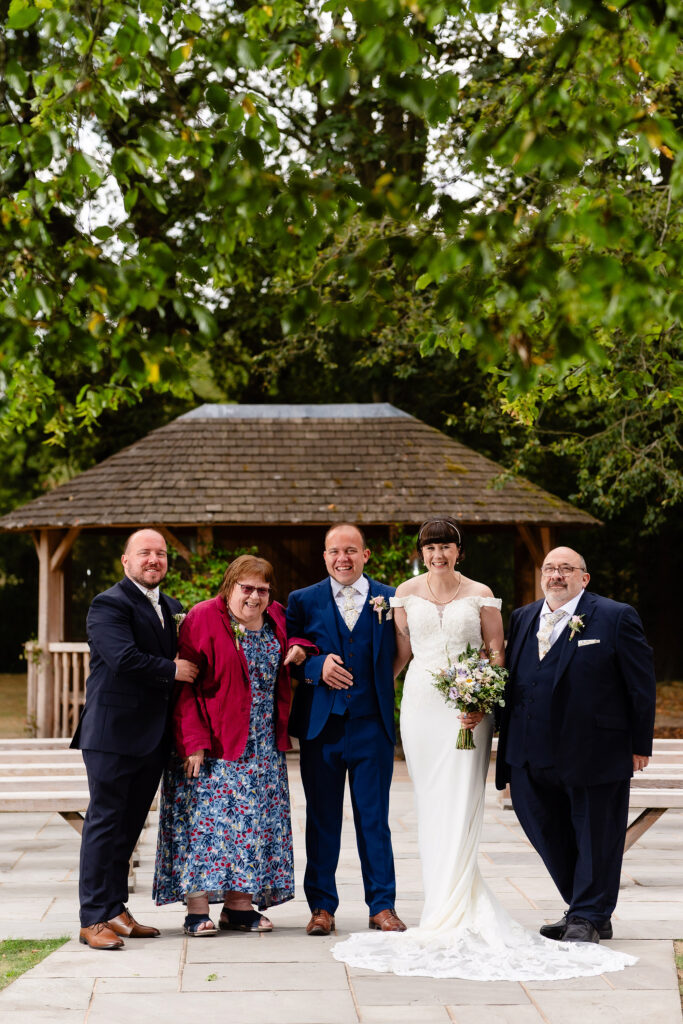 Bride and groom with a group of guests in front of the wooden gazebo, Cheshire wedding photographer