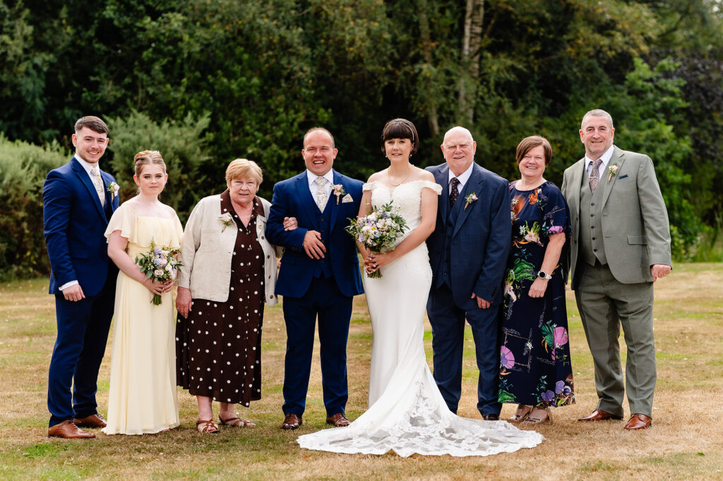 Bride and groom with a larger group on the lawn, the bride's lace train spread out in front