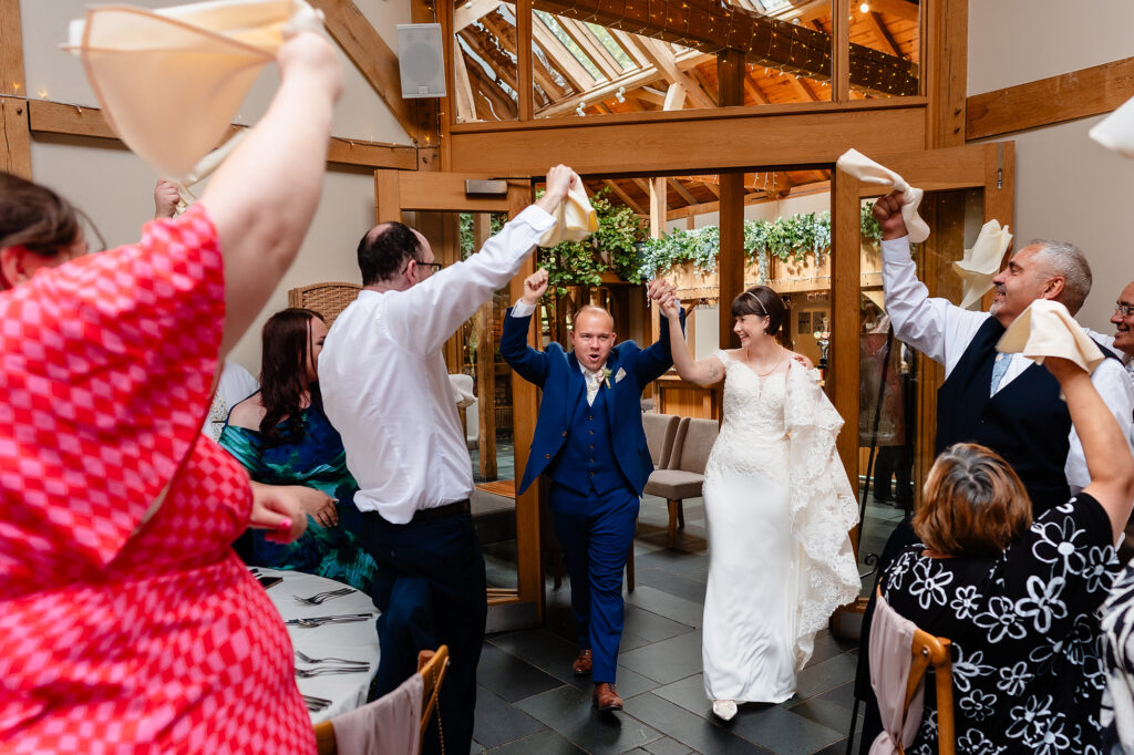 Bride and groom making their entrance into the wedding breakfast as guests wave their napkins in the air at The Oak Tree of Peover