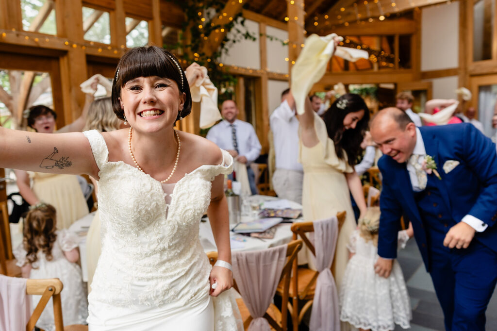 Bride grinning straight at the camera during the napkin waving entrance, groom laughing behind her
