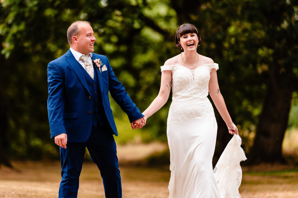 Bride and groom laughing as they walk hand in hand under the trees at The Oak Tree of Peover