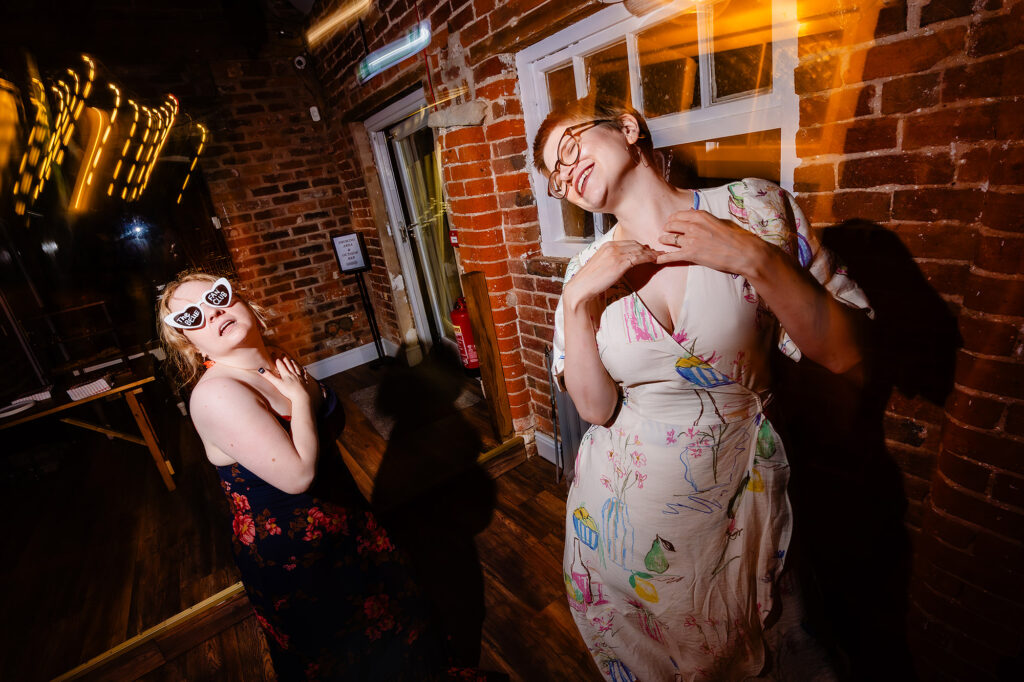 Two guests striking a pose on the dance floor, one in heart shaped sunglasses