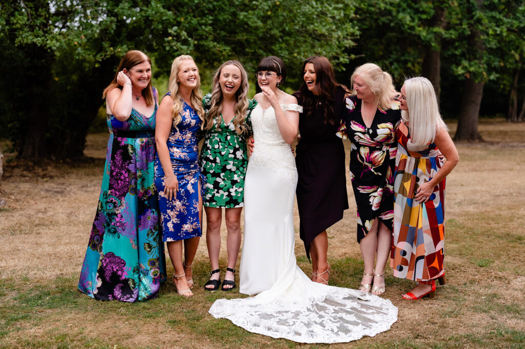Bride laughing with a group of guests in colourful dresses on the lawn
